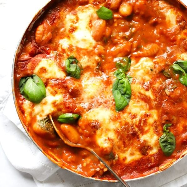 A large pan of cooked Gnocchi Bake with mozzarella and basil on top, with a spoon ready to serve.