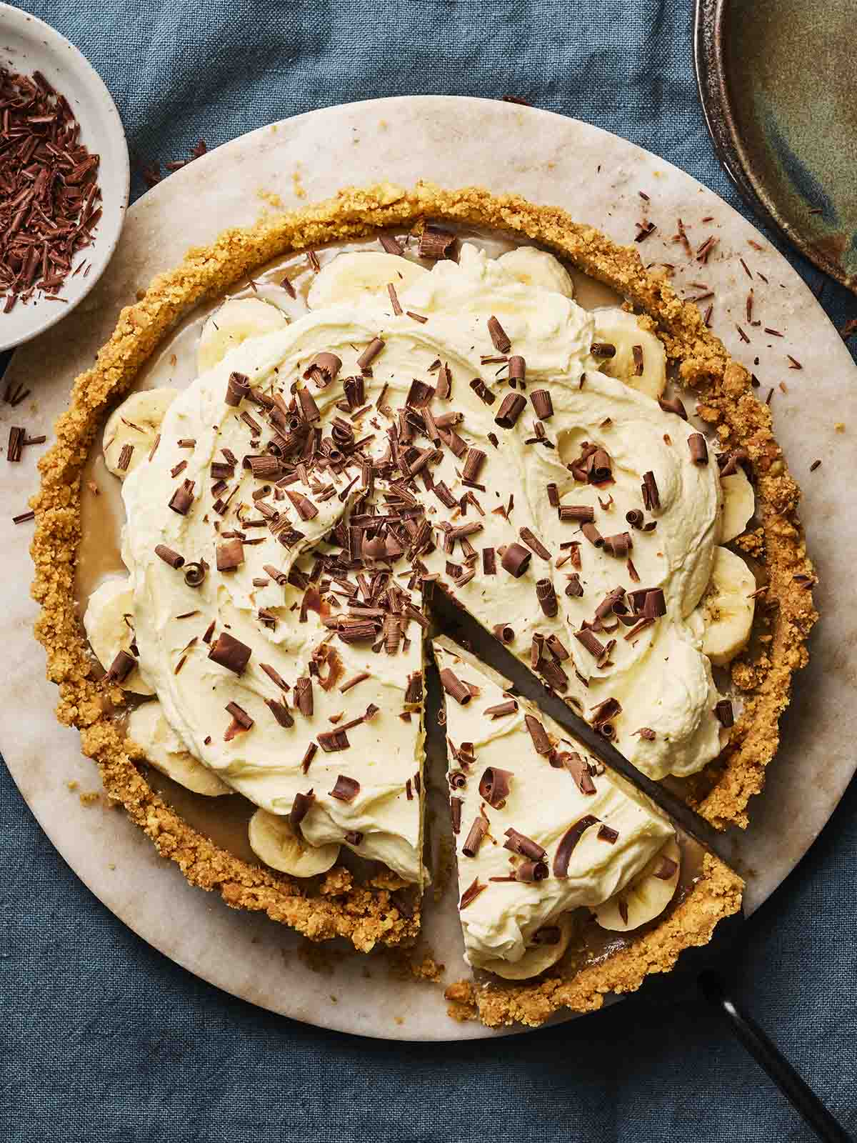 A pie made with bananas, caramel and cream with a biscuit crust and grated chocolate on top, ready to eat.