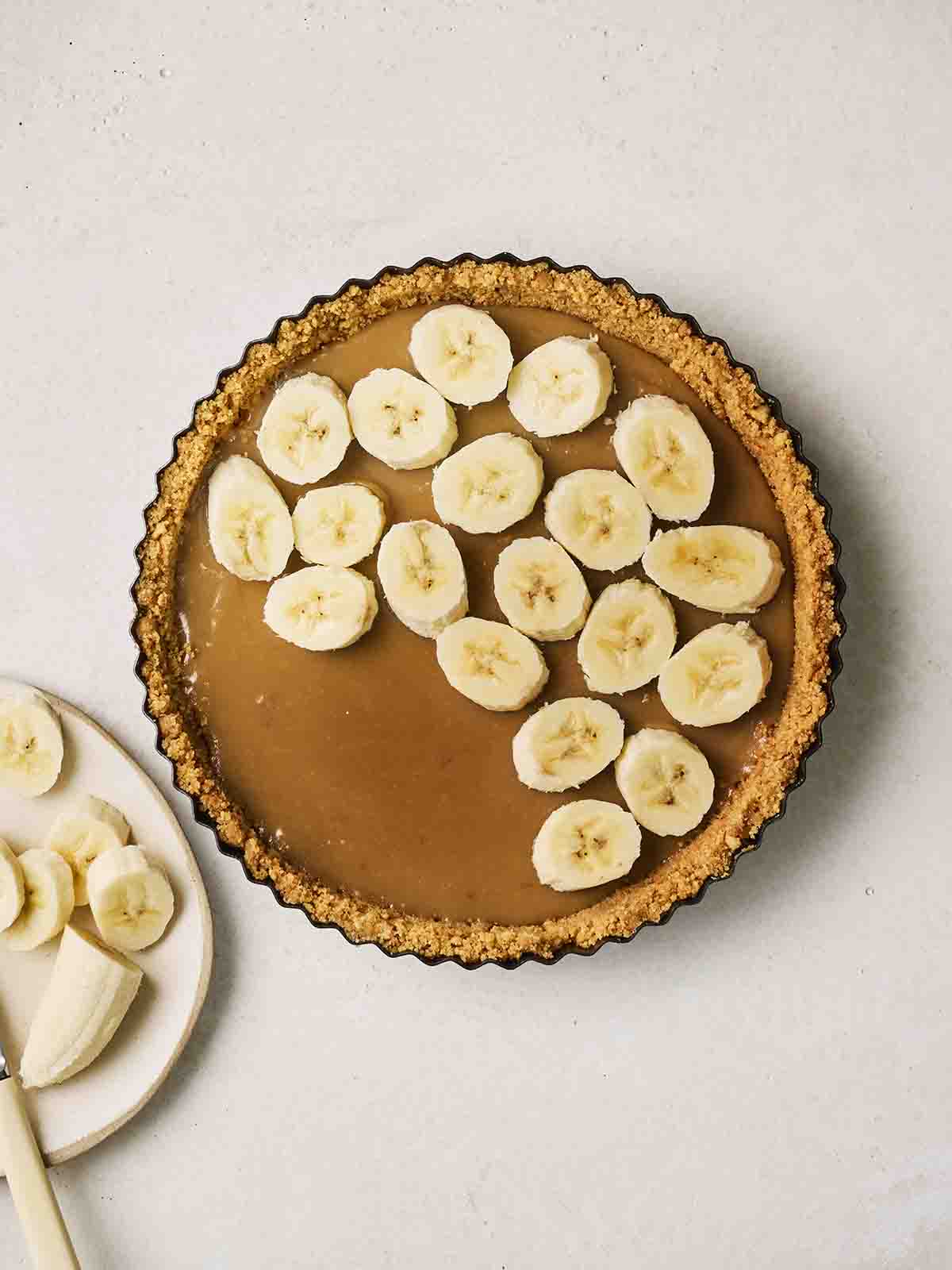 A banoffee pie with banana slices being filled on top.