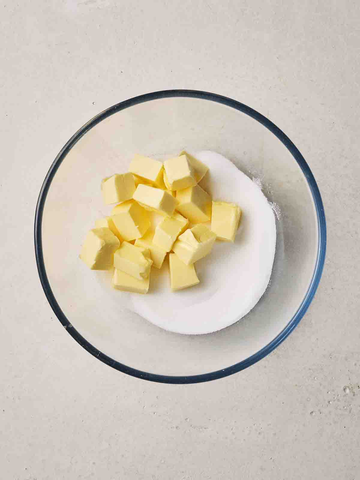 Cubes of butter and sugar in a glass bowl together.