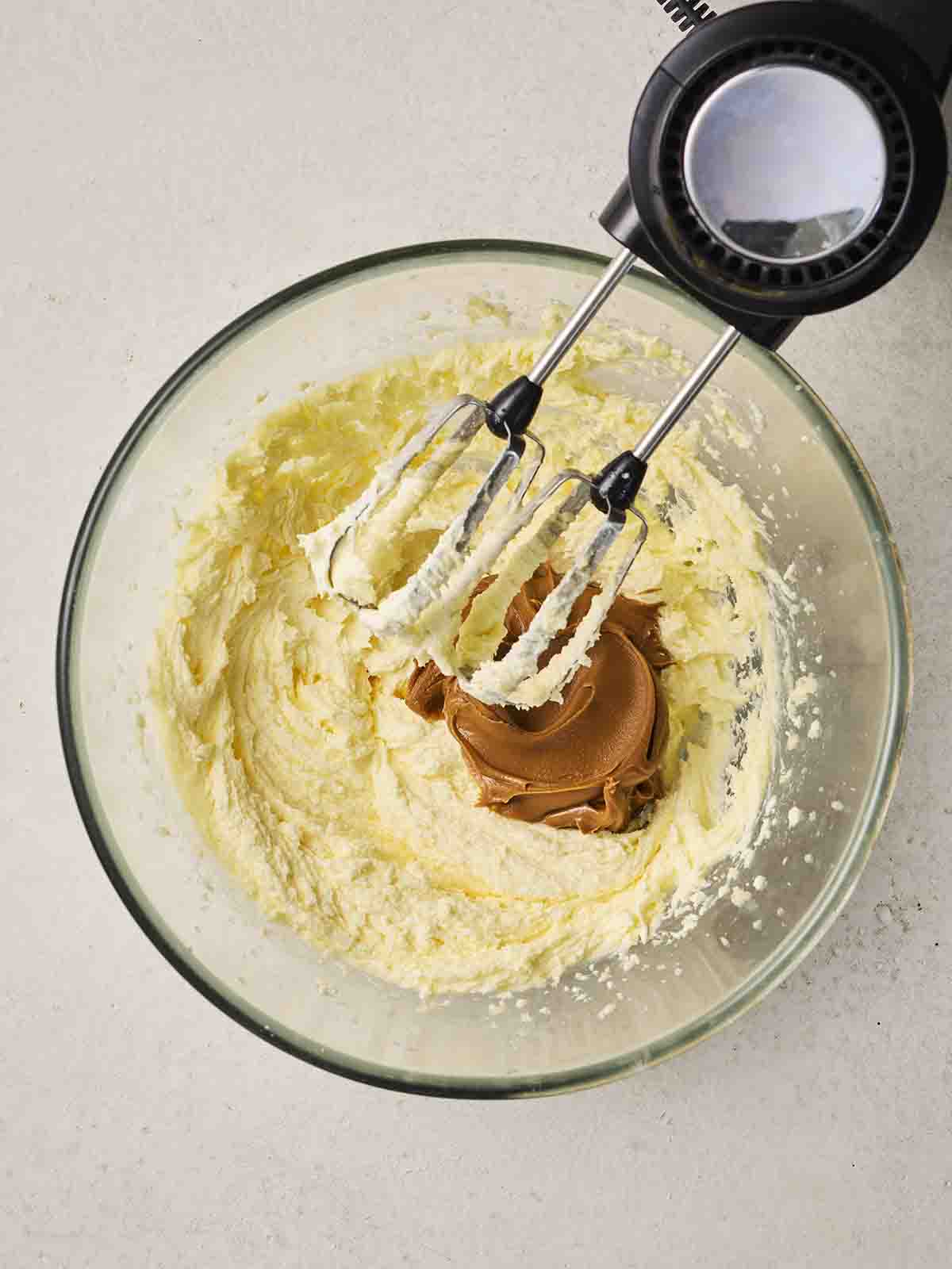 Butter and sugar whisked together in a bowl, with Biscoff spread in the middle.