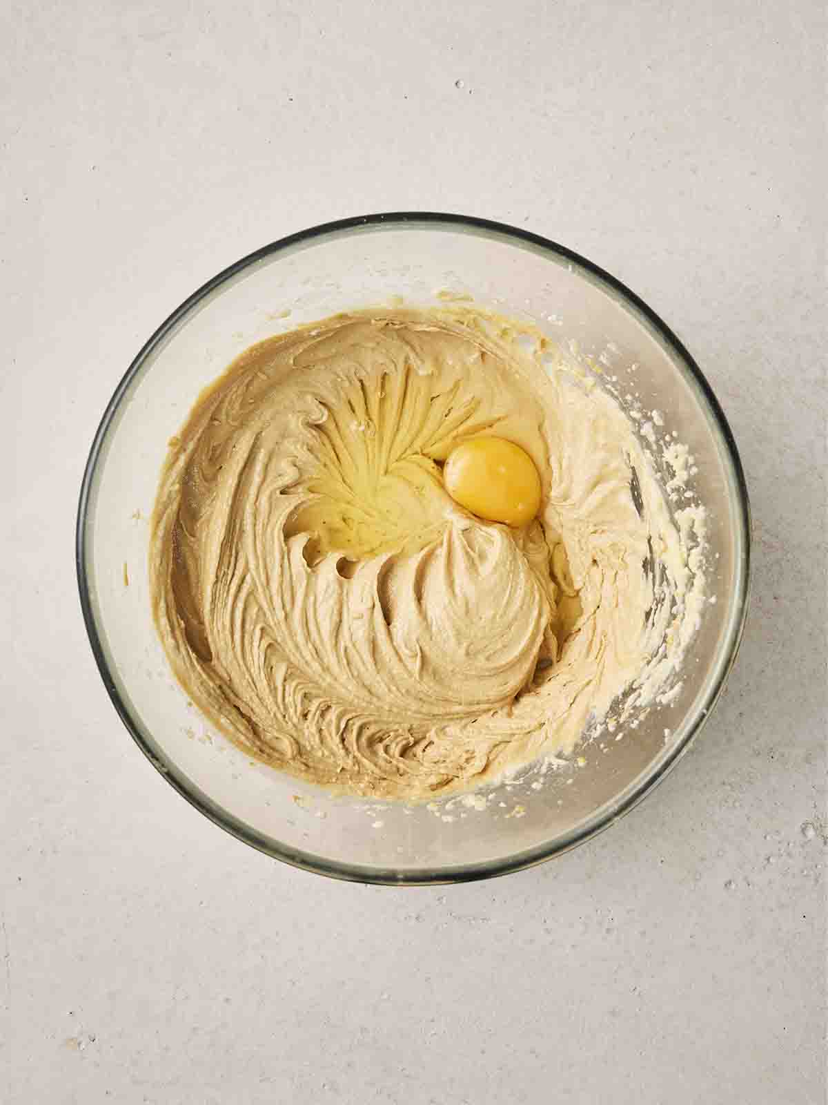 An egg on top of a cake batter in a glass bowl, ready to mix in.