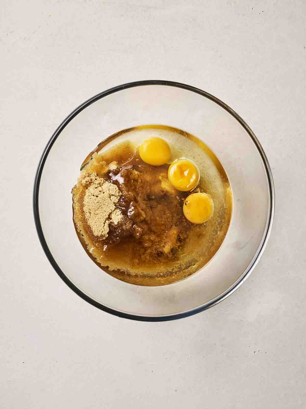 Three eggs in a glass bowl with sugar and oil.