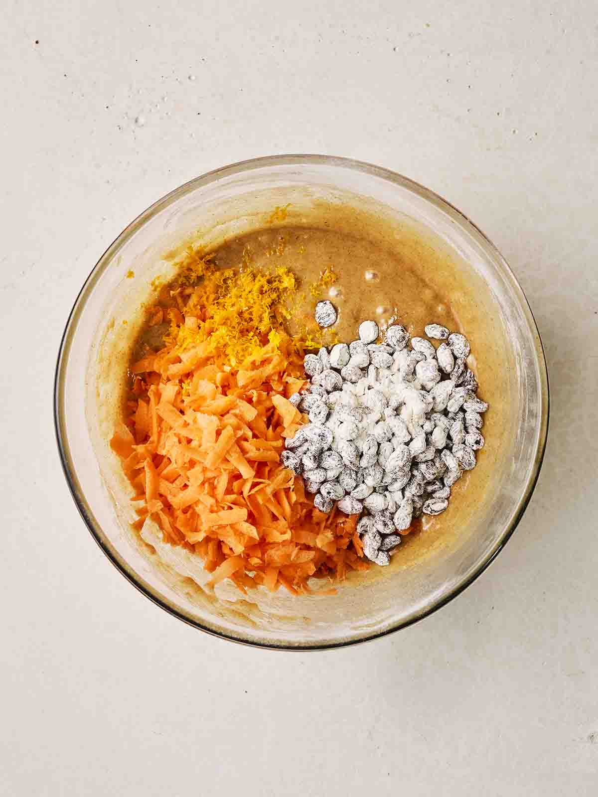 Grated carrots and raisins on top of a bowl of cake batter for step 4 in the recipe for Carrot Cake.
