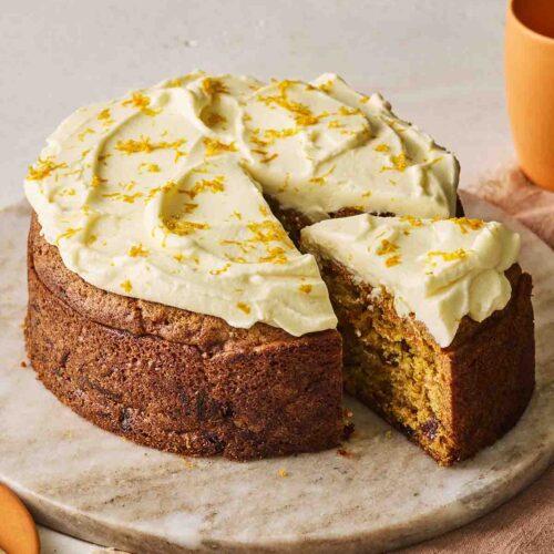 A simple carrot cake on a cake dish with a slice cut out.