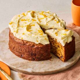 A slice of carrot cake being pulled from the rest of the cake, ready to eat.