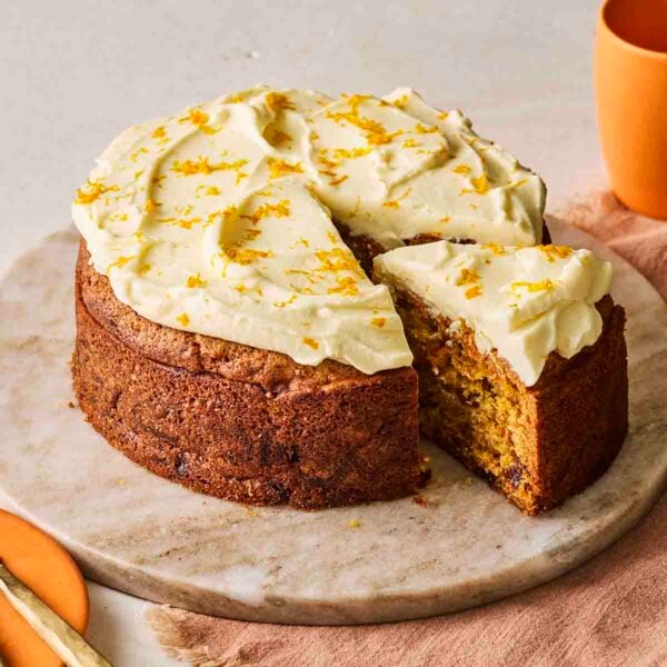 A slice of carrot cake being pulled from the rest of the cake, ready to eat.
