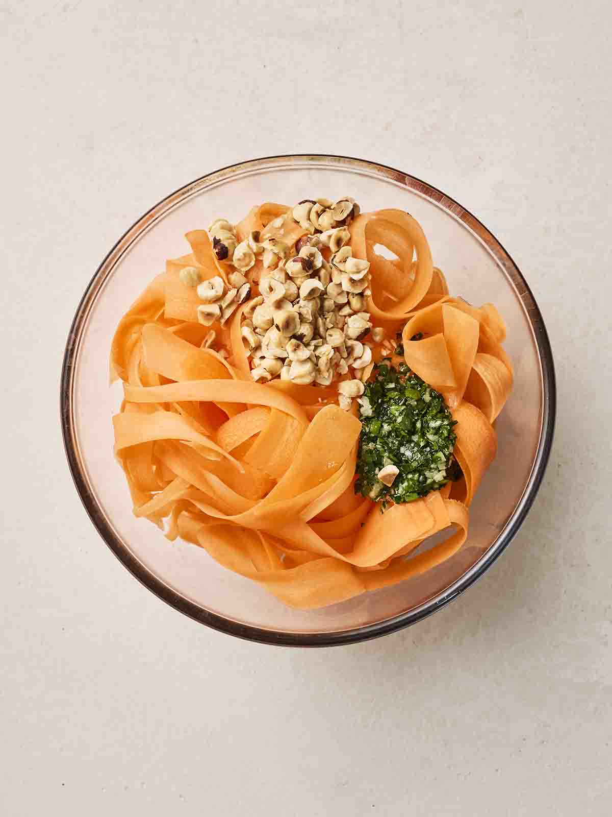 A glass bowl with carrot salad ingredients, ready to mix.