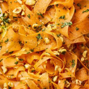 A close up of carrot ribbons in a salad with nuts and dressing.