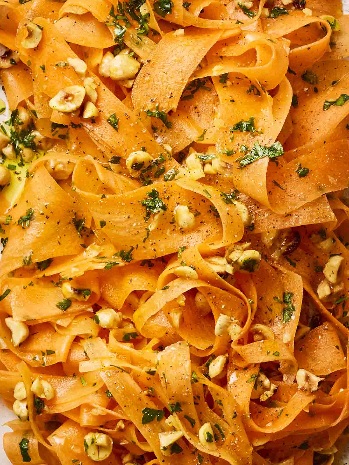 A close up of carrot ribbons in a salad with nuts and dressing.