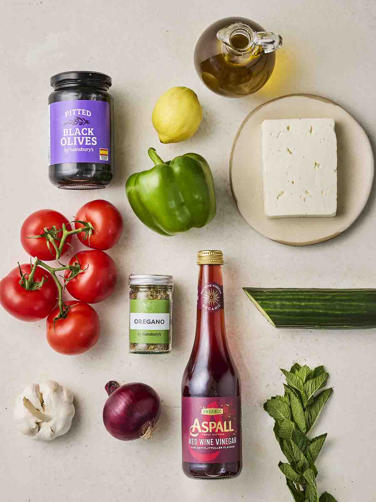 The ingredients for making a simple Greek Salad laid out on a white counter.