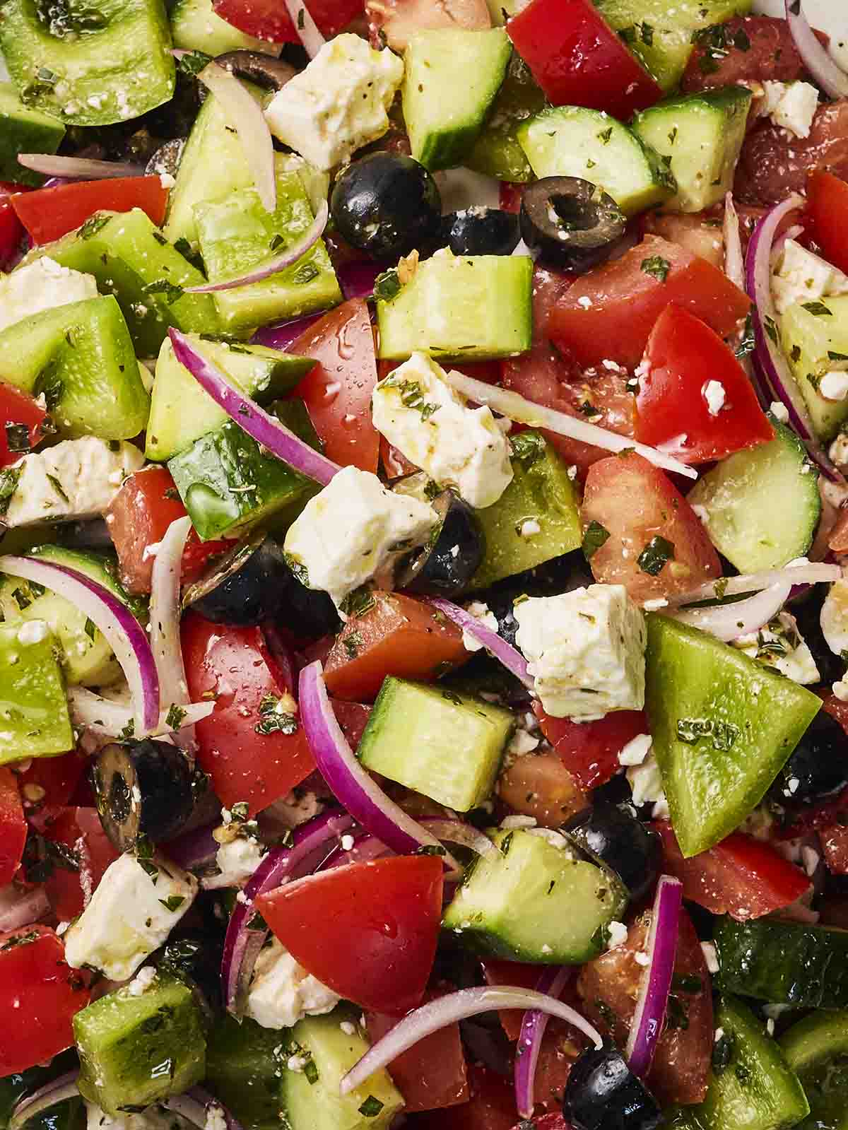 A close up of chopped salad with Greek inspiration, with chunks of feta, cucumber, tomatoes, onion and green peppers.