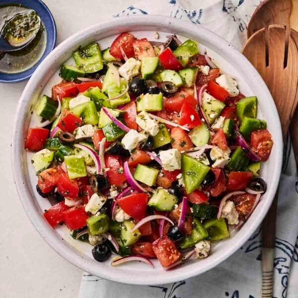 A white bowl with chopped Greek Salad, with utensils around the side.
