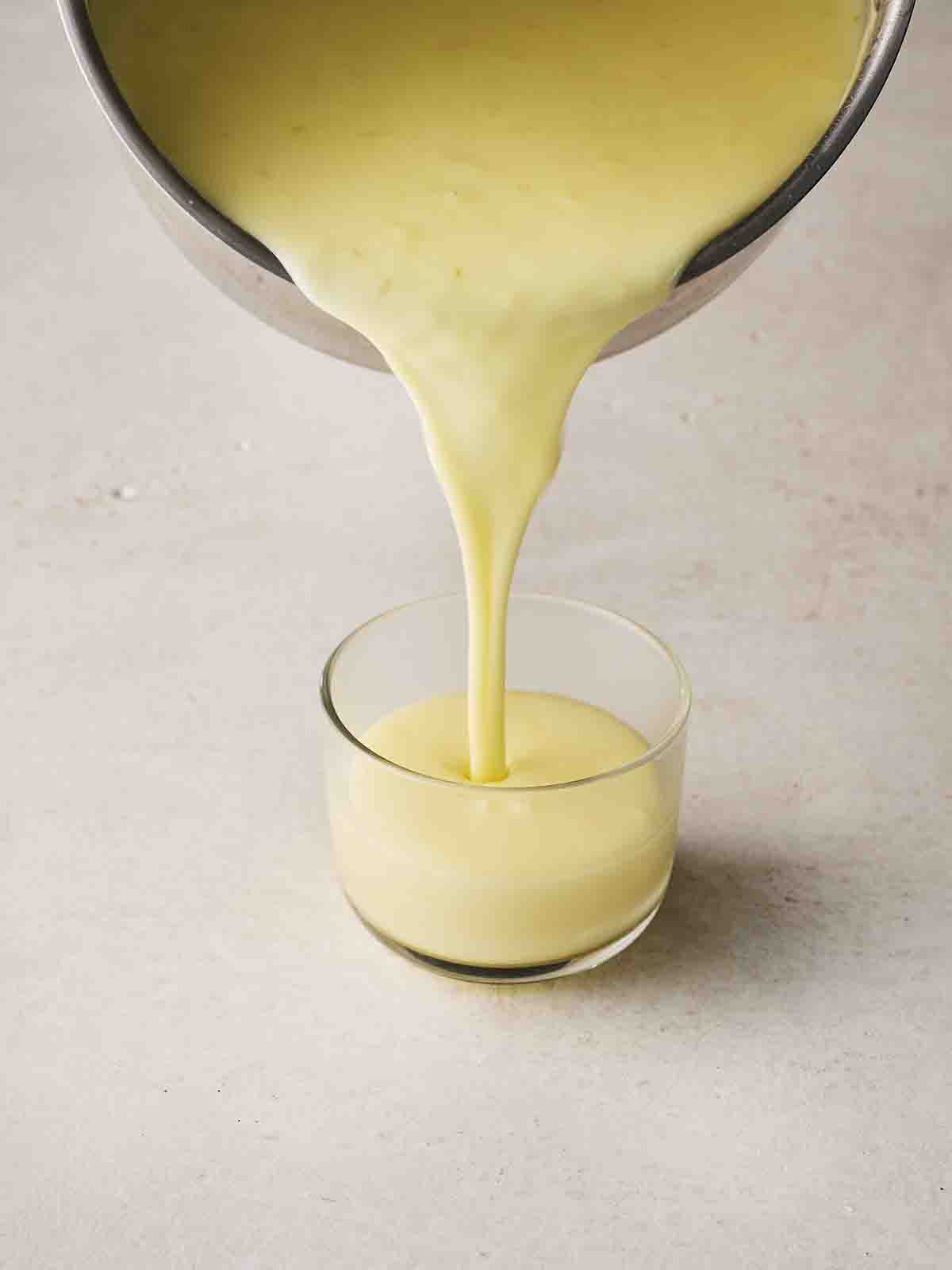 Lemon Posset being poured into a glass dessert ramekin, ready to set.