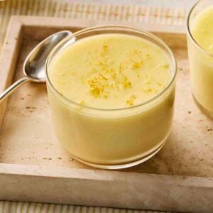 A small glass of Lemon Posset dessert, with zest on top and a spoon to the side, ready to eat.