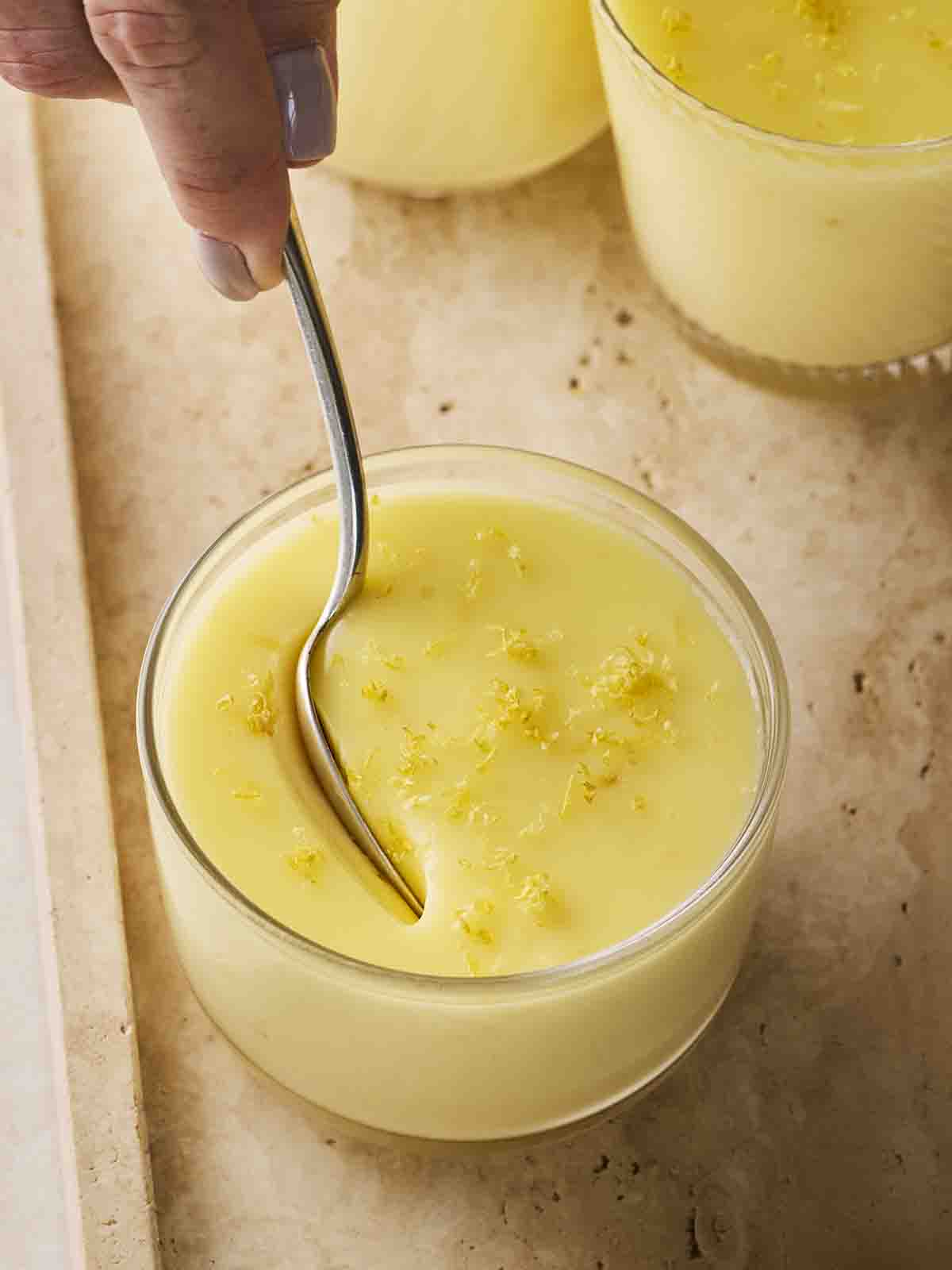 A spoon digging into a small lemon posset desserts.