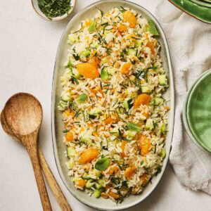 A platter with a rice salad on top, ready to serve out onto plates, with salad serves at the side.