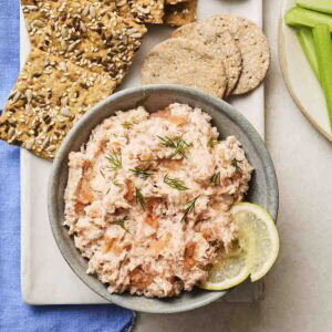 A bowl of homemade Salmon Pate on in a bowl, on a plate with crackers and celery to the side.