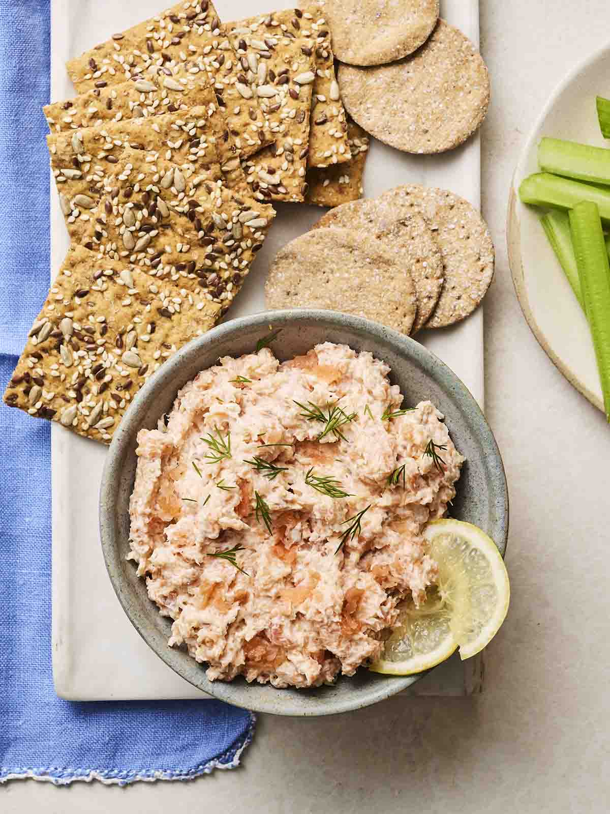 A bowl of Salmon Pate with wedges of lemon on a platter with crackers and celery off to the side.