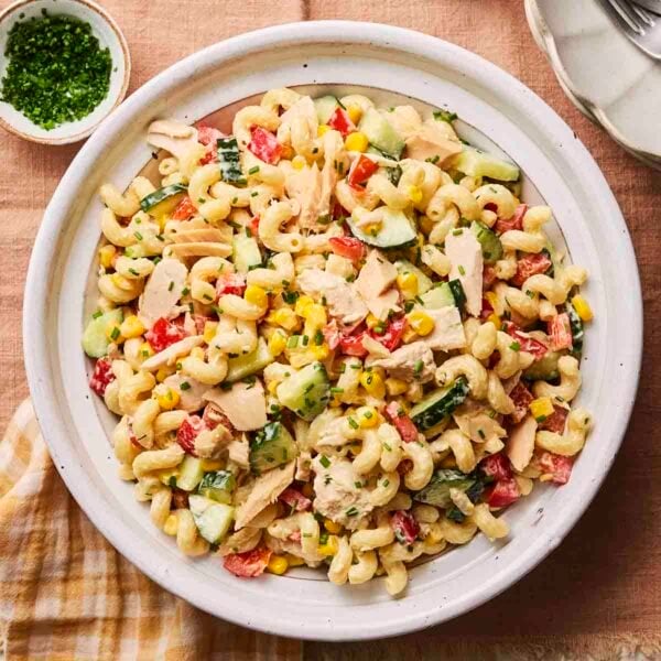 A white plate filled with tuna pasta salad, with dressing to the side.