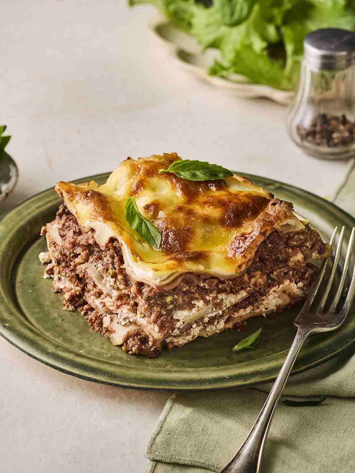 A slice of Vegetarian Lasagne on a green plate with a fork, ready to eat.