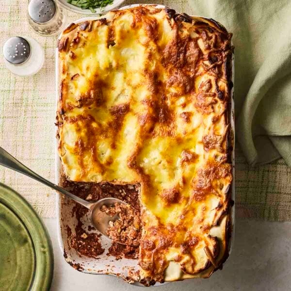 A cooked veggie lasagne with a slice missing, on a table with a spoon, serving from the oven dish.
