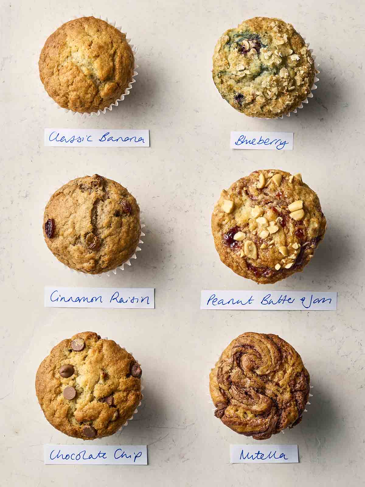 An assortment of banana muffins on a white surface with different flavours, with labels underneath.