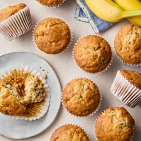 An assortment of baked Banana Muffins on a white surface and plate, ready to eat.