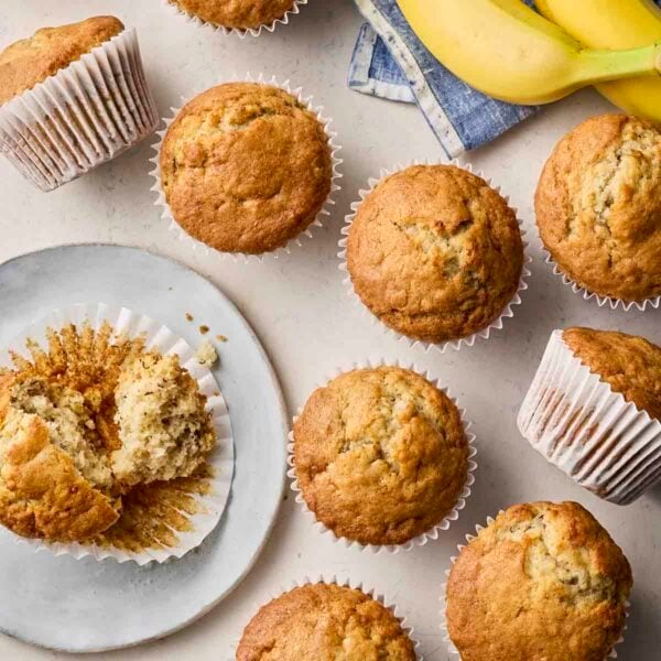 An assortment of baked Banana Muffins on a white surface and plate, ready to eat.