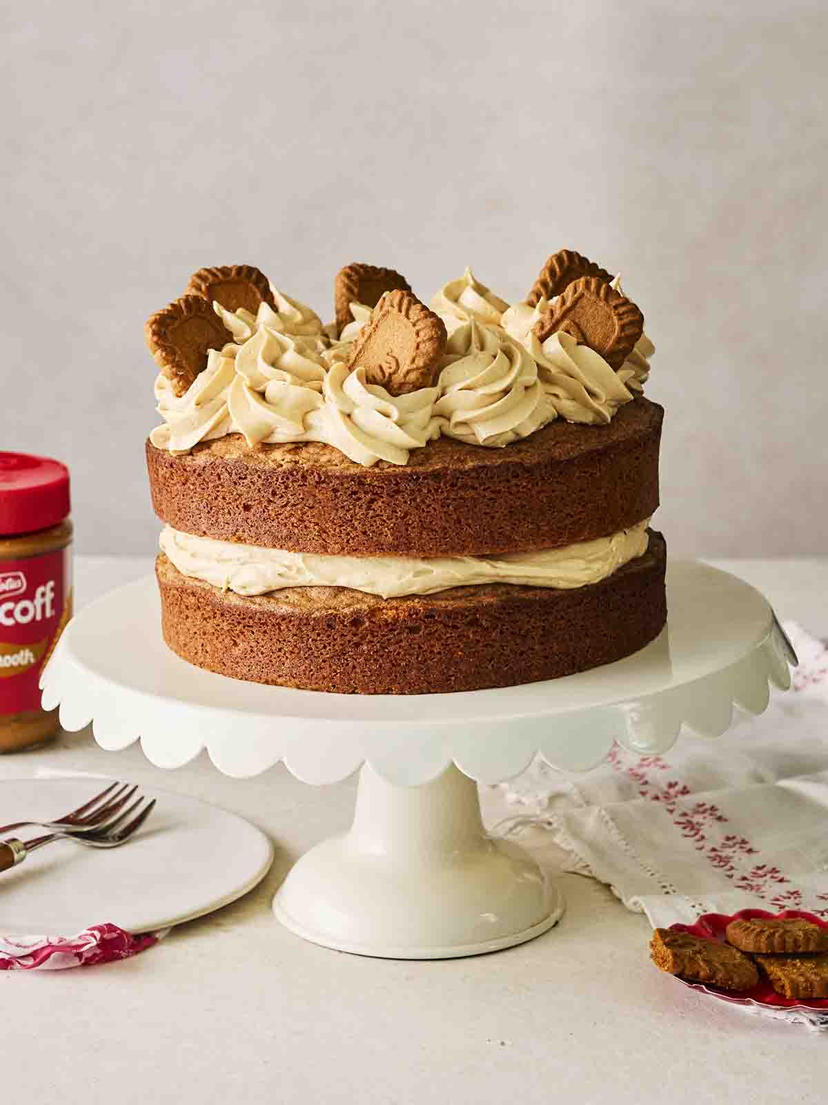 A large two layer biscoff cake on a cake stand with biscuits on top.
