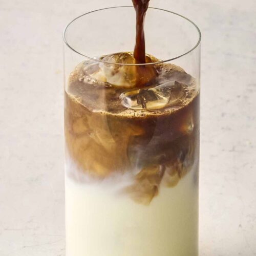 Coffee being poured into a glass of iced milk to make Iced Coffee.
