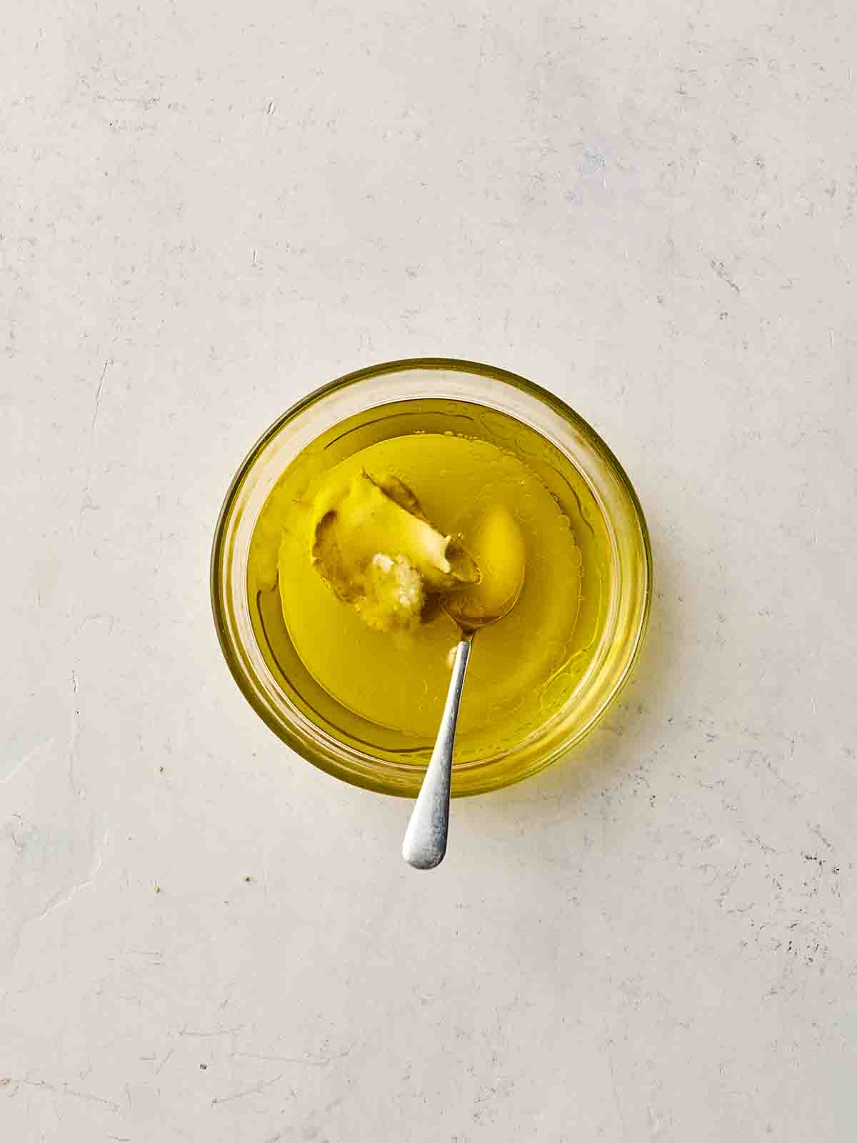Oil and other ingredients in a bowl, with a spoon, ready to mix into a dressing.