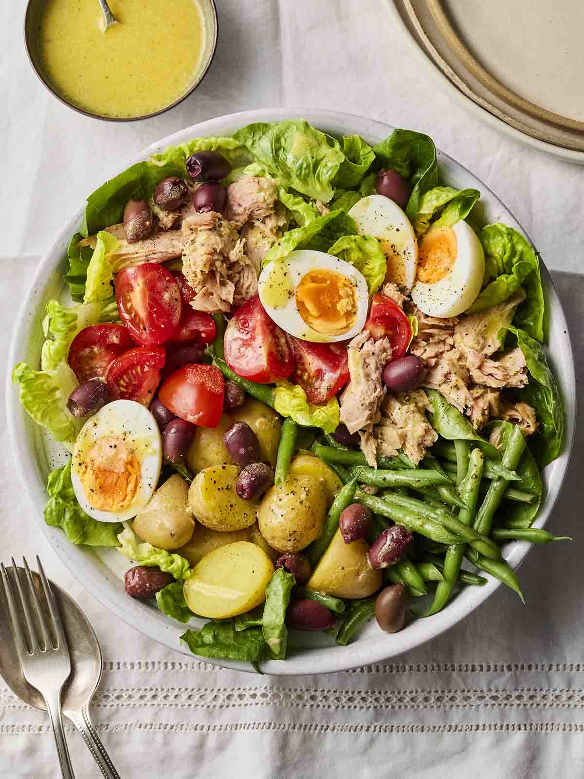 A plate filled with salad, egg, tuna, green beans, olives and potatoes, with cutlery to the side.