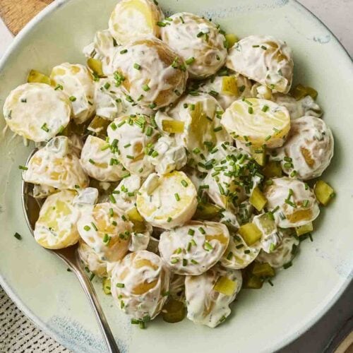 Potatoes with creamy dressing in a bowl with a spoon on a table.