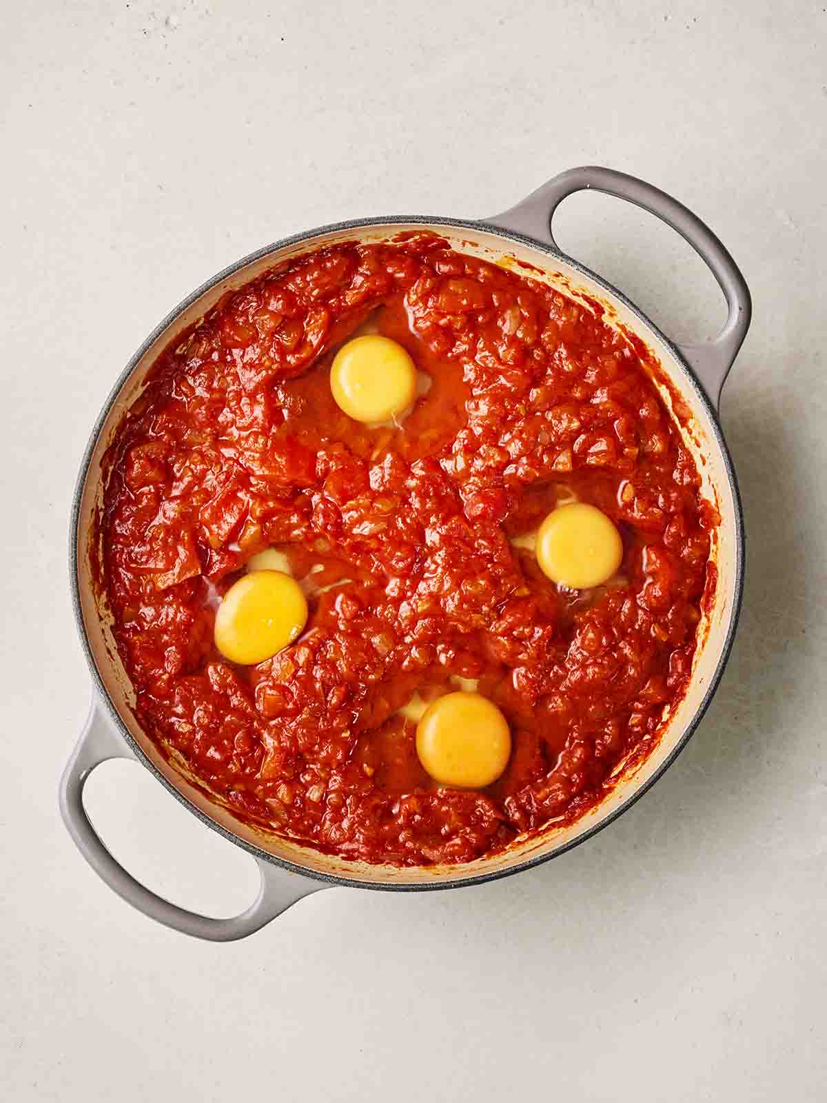 A pan of tomatoes with four eggs inside, not yet cooked.