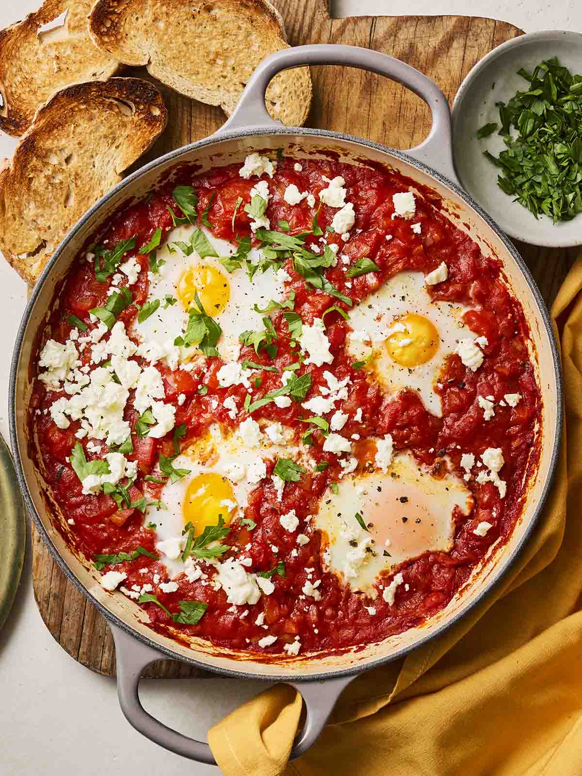 A large pan filled with Shakshuka, a tomato stew with eggs, with toasted bread around the sides.