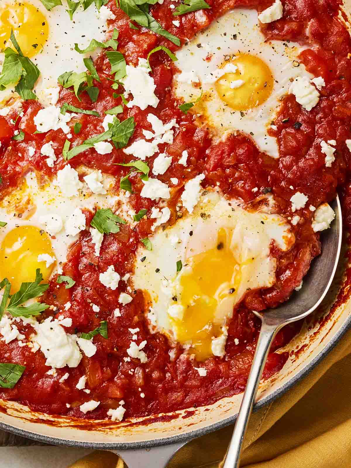 A close up of a pan with a tomato sauce and eggs on top, with a spoon to serve.