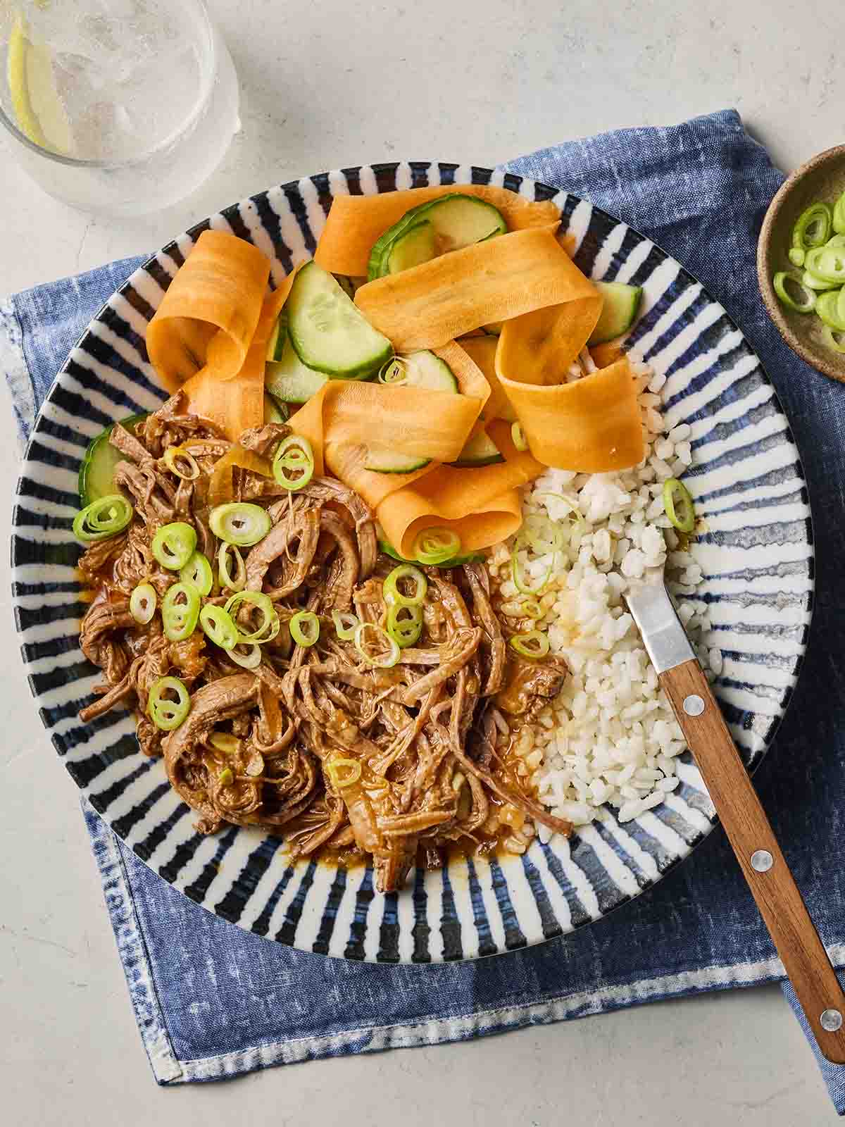 A blue and white plate filled with slow cooked shredded Korean Beef with rice and carrots and cucumber.