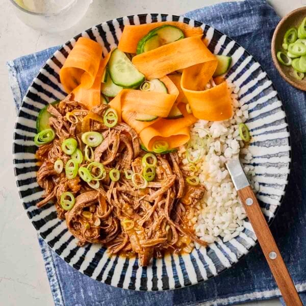 A plate filled with shredded Korean Beef, rice and vegetables, with a fork on the plate and a blue placemat underneath.