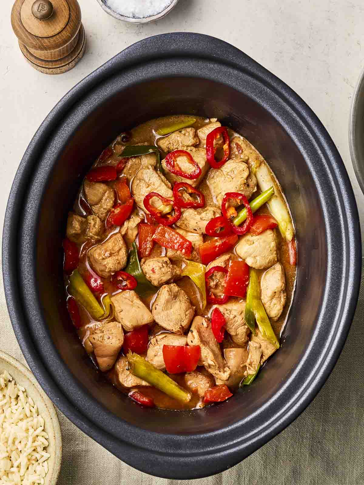 A slow cooker pan on a table, with a cooked chicken and sauce dish inside.