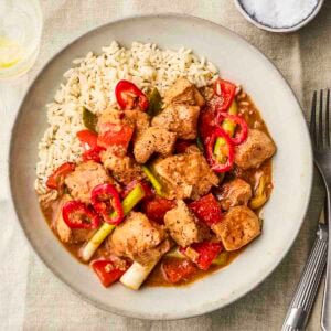 A plate with rice and Salt and Pepper Chicken with peppers on, with cutlery to the side.