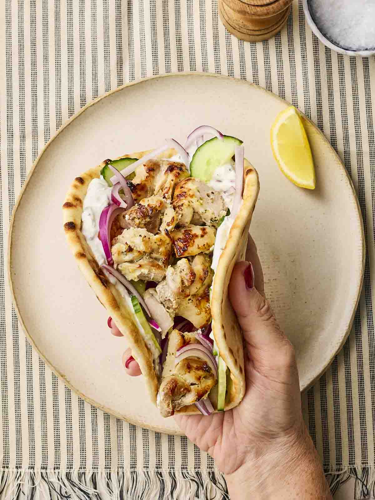 A handheld chicken souvlaki over a plate.