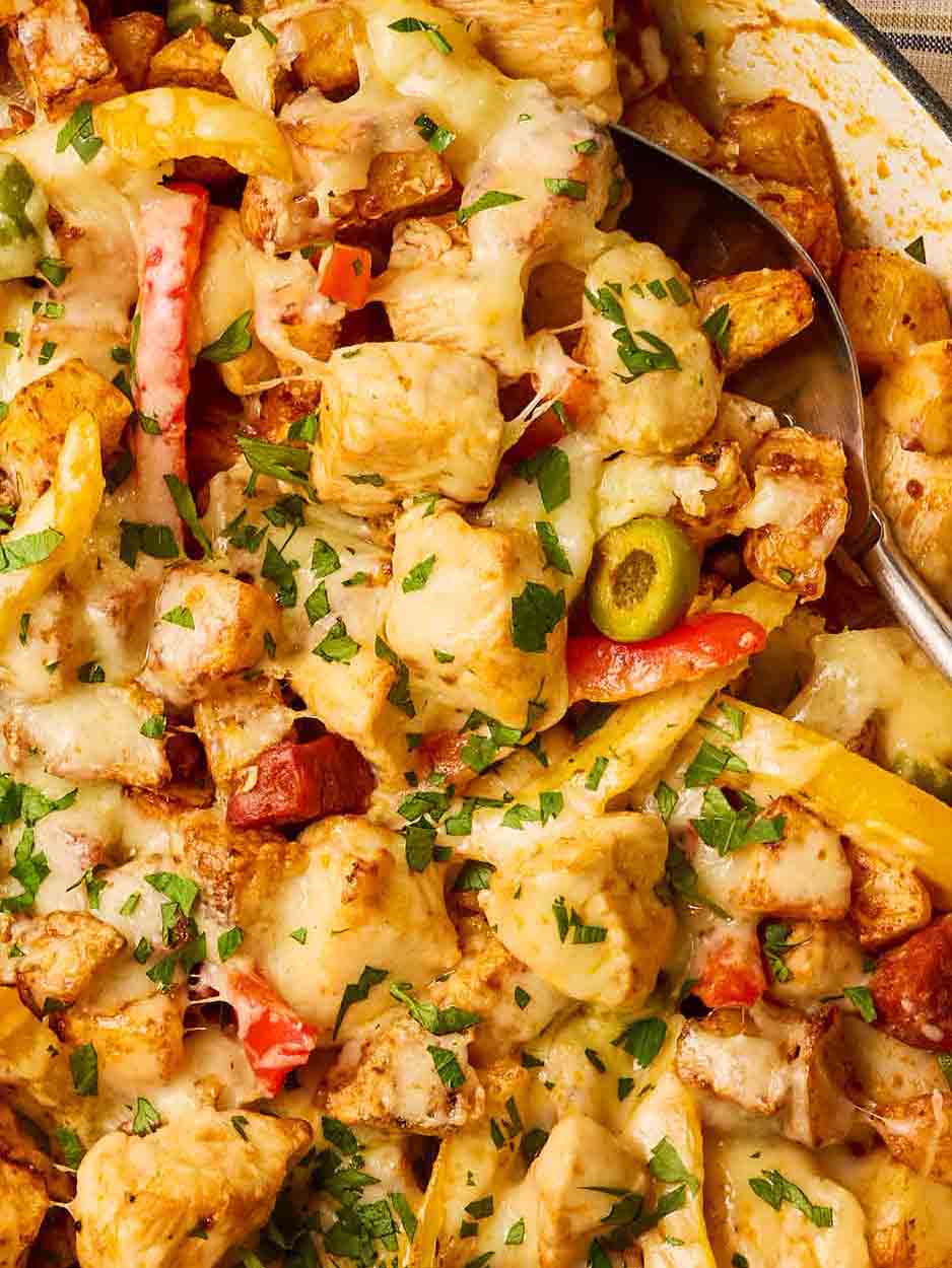 A close up of pan of chicken, chorizo, olives, peppers and potatoes.