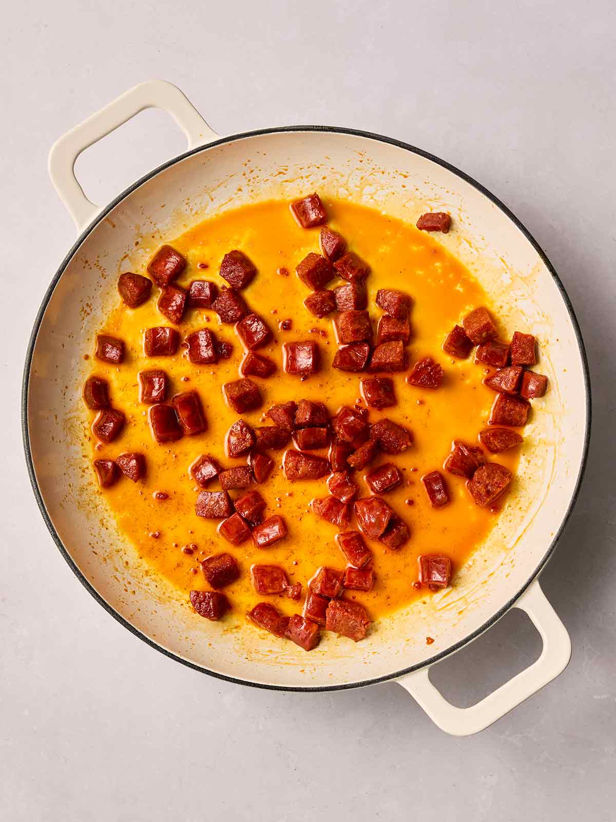 A white pan filled with cubes of chorizo, frying with the oils released.