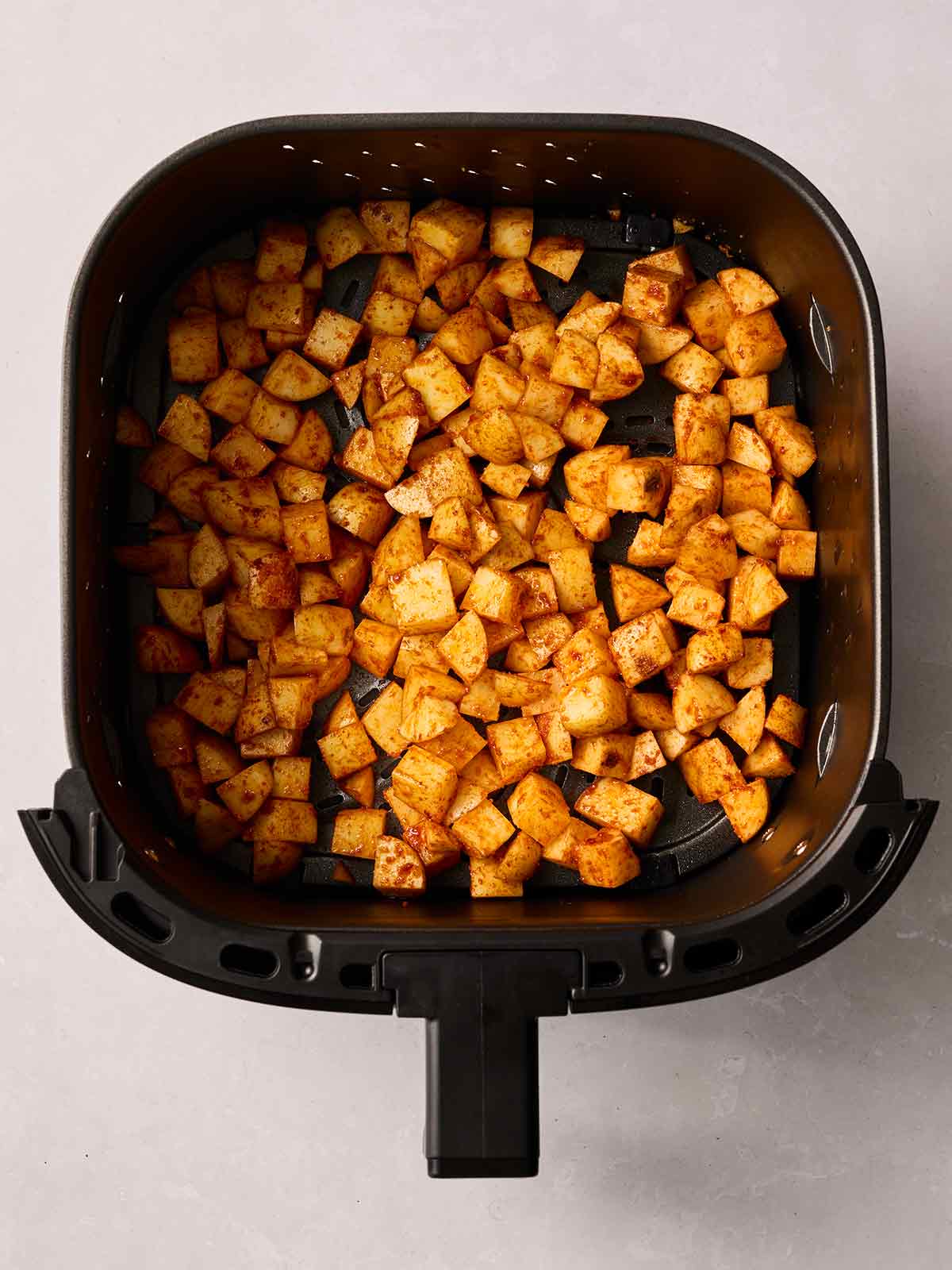 An air fryer pan with cubed potatoes inside, coated with sweet smoked paprika.