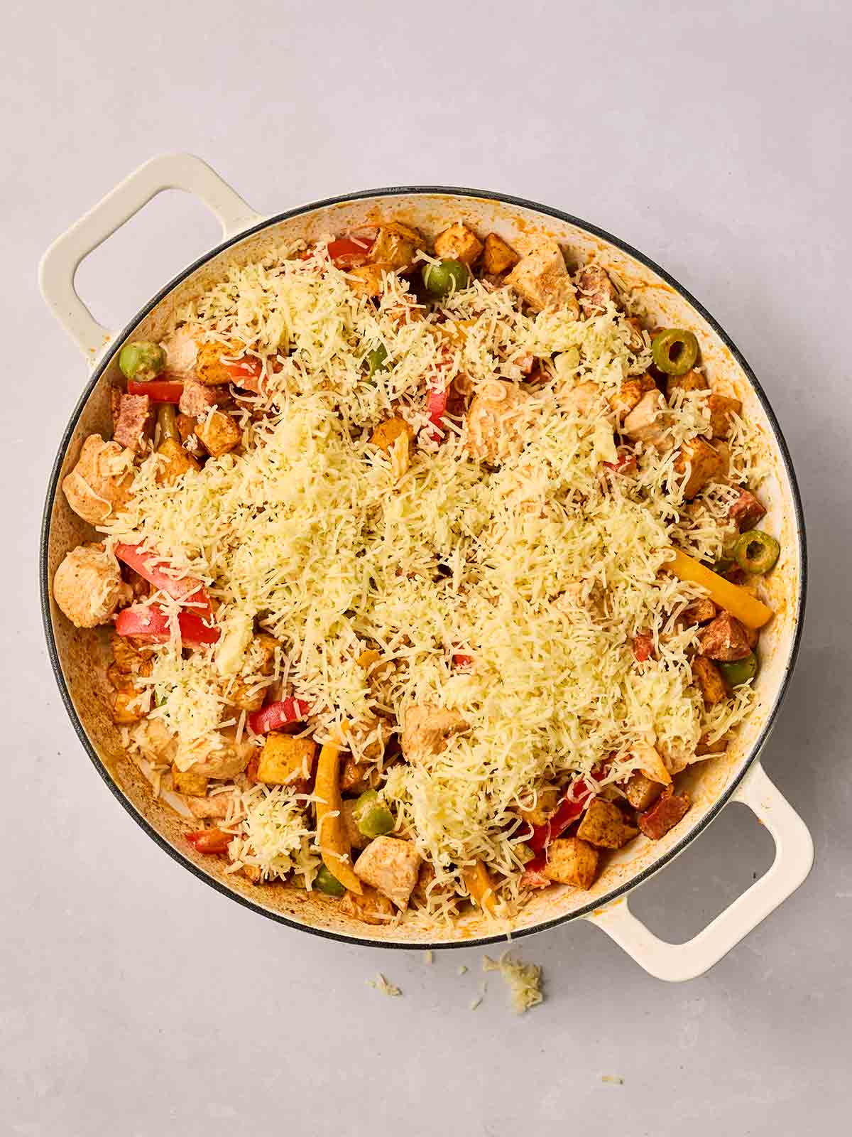 Grated cheese over the top of a pan with chicken, chorizo and air fryer potatoes.