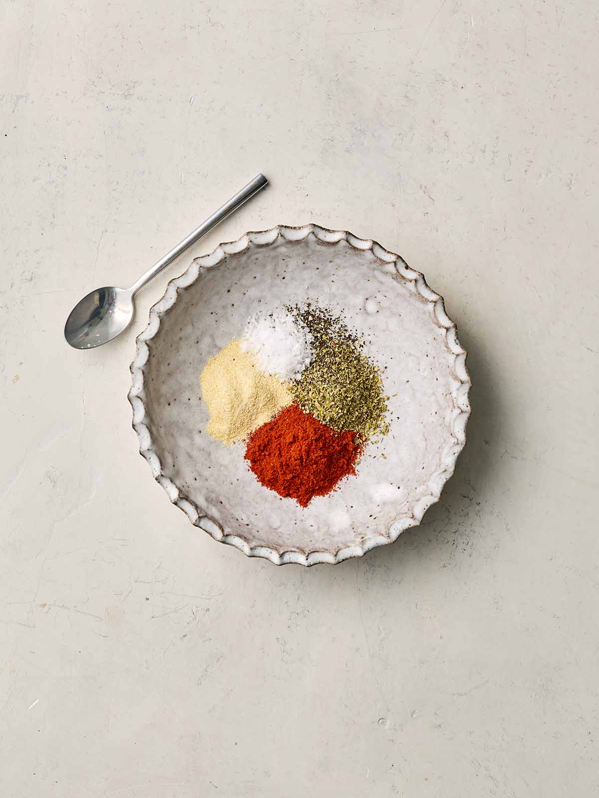 A white bowl with a spice mix inside and a spoon to the side.