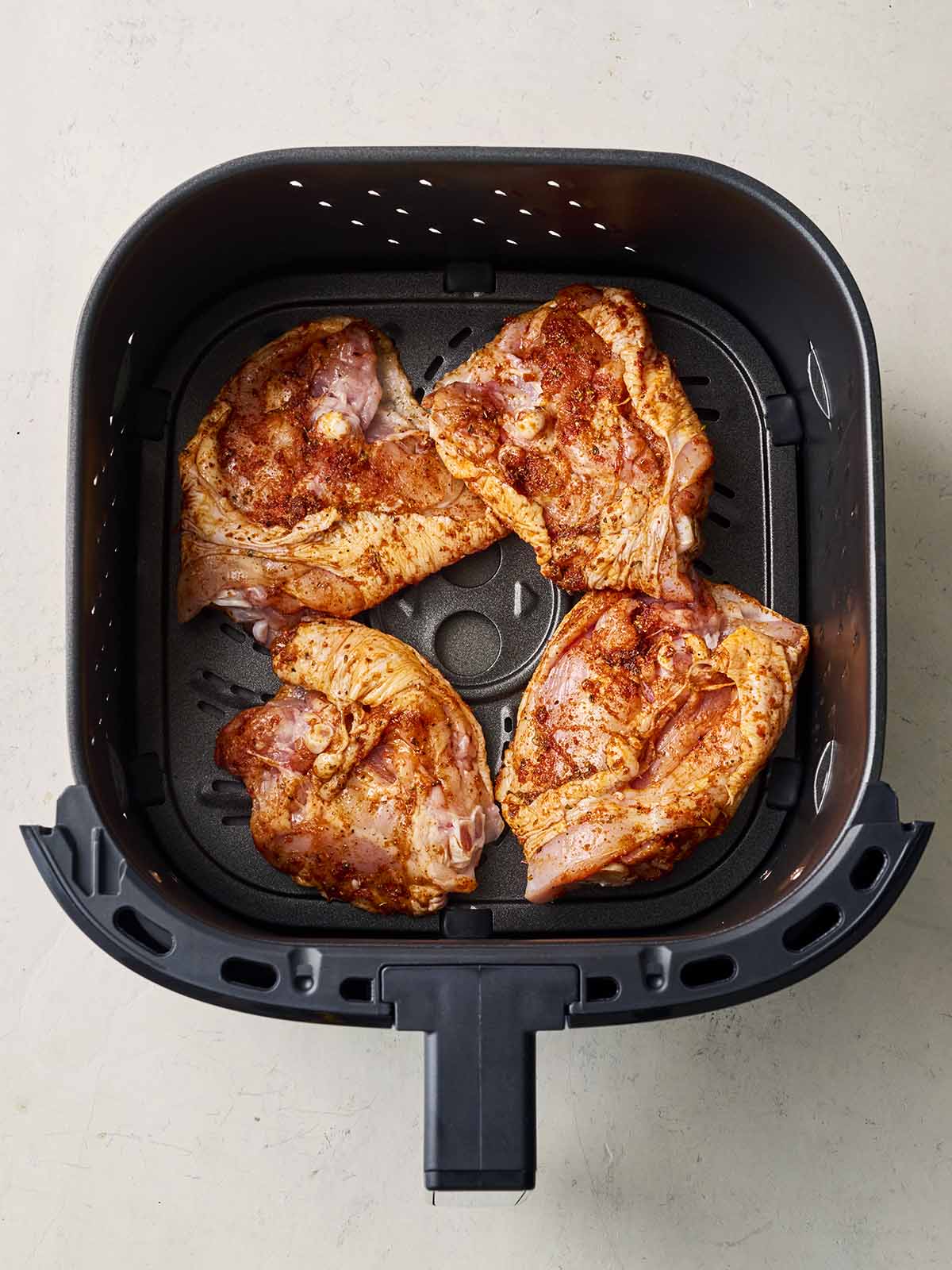 An air fryer grill with four marinaded chicken thighs, uncooked, inside.
