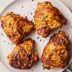 A white plate with four cooked, coated chicken thighs, ready to eat.