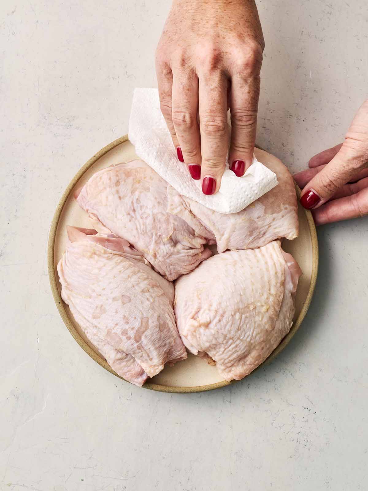Two hands dabbing chicken thigh skin with a paper towel.
